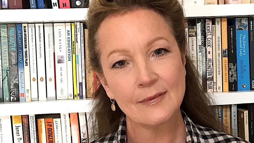 Charlie Lee Potter stands in front of a bookcase, wearing a checked shirt